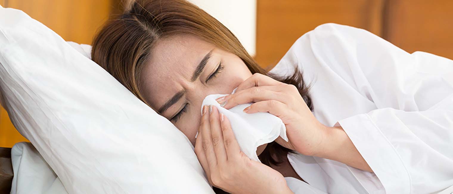 sick woman blowing her nose in bed
