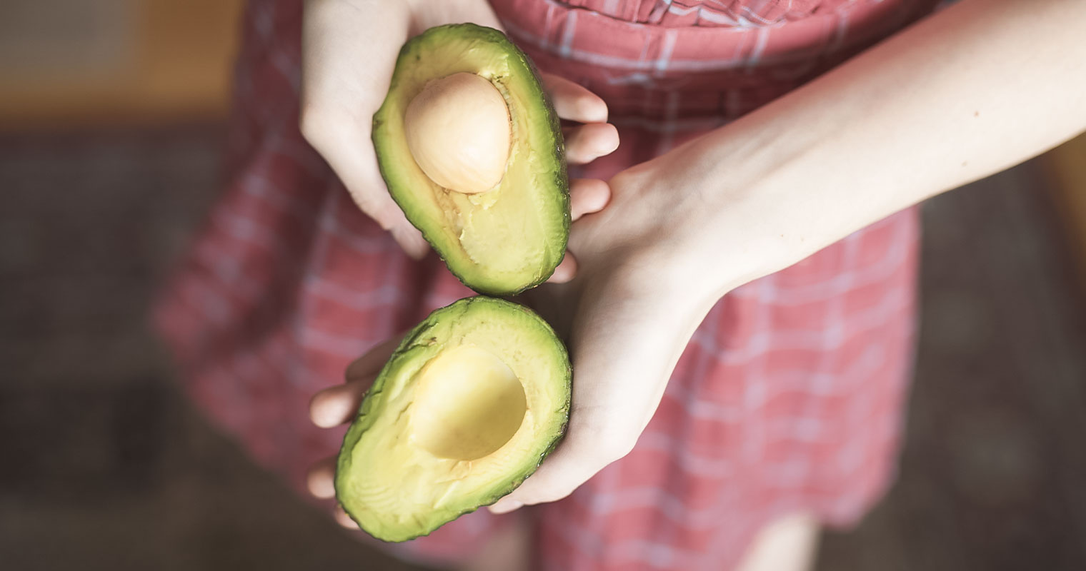 Girl holding an avocado cut into half showing the avocado seed